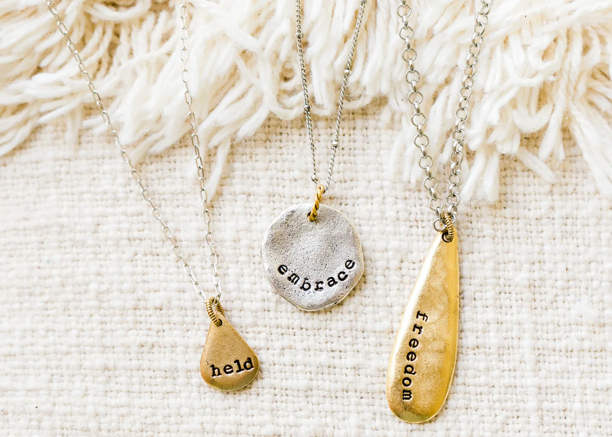 A gold hand-stamped pendant necklace resting on a linen surface